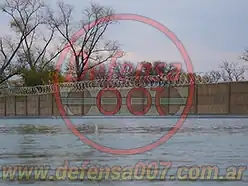 Instalación de concertina helicoidal cruzada sobre muro premoldeado. Delante piletones de tratamiento de agua. Parque logístico.