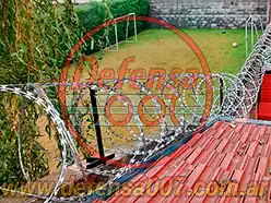 Instalación de concertina helicoidal cruzada sobre muro y techo. Al fondo una cancha de fútbol.